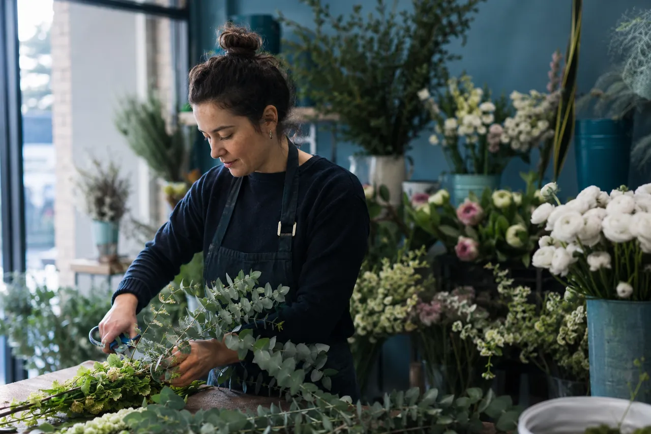 A florist trimming eucalyptus stems at a workbench in her shop