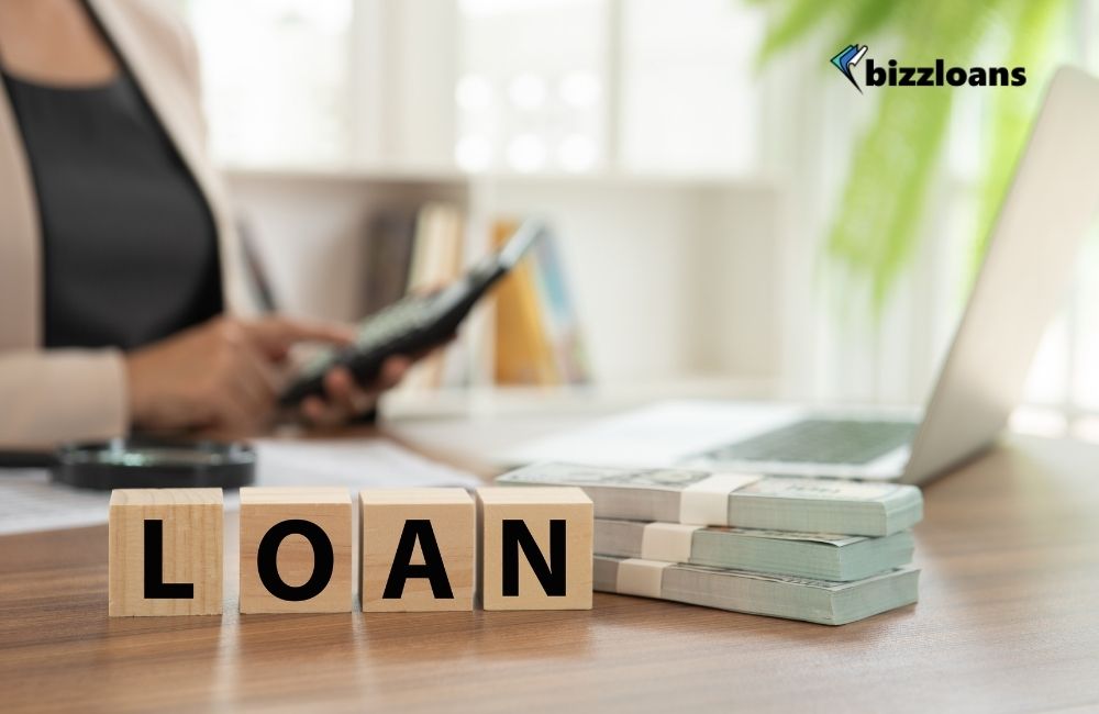 how-to-get-a-business-loan-in-5-easy-steps-10 business loan concept; woman using calculator in front of laptop with cash and word "loan"