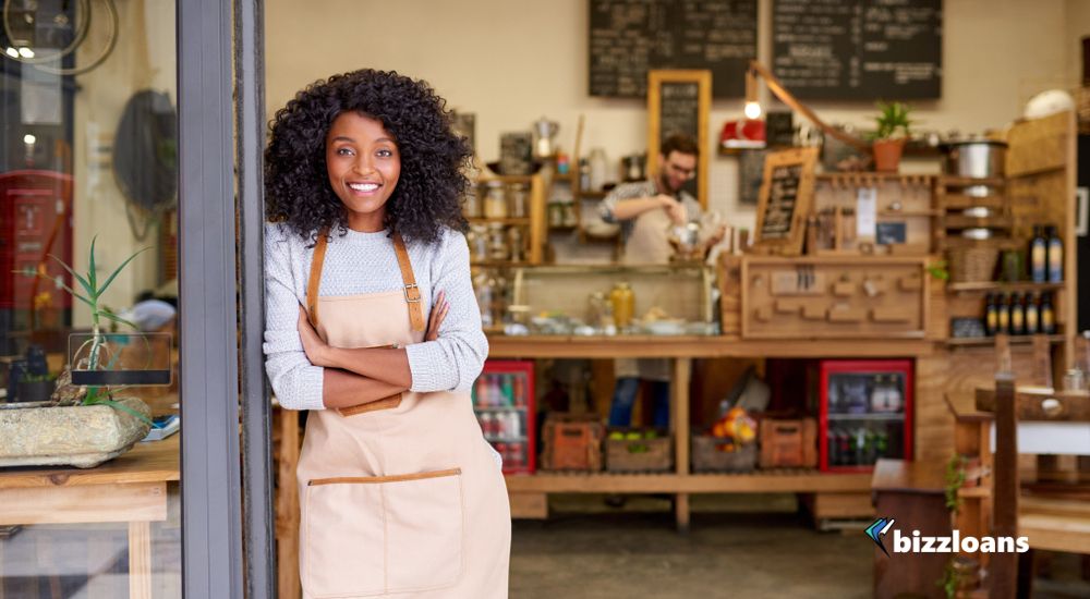merchant-cash-advance-loans-in-australia Portrait of a smiling young African American barista leaning with her arms crossed on the door of a trendy cafe